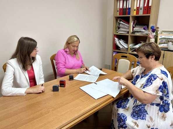 Zdjęcie przedstawia trzy kobiety siedzące przy stole; wójt gminy Gardeja podpisuje dokumenty, obok siedzi skarbniczka gminy; kierownik PCPR w Kwidzynie przegląda dokumenty