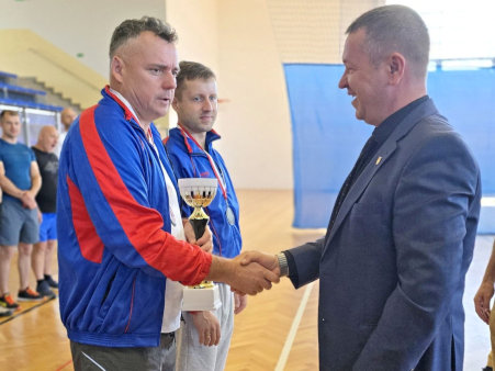 Starosta Powiatu Kwidzyńskiego podaje dłoń mężczyźnie, który trzyma w dłoni puchar, obok niego stoi drugi mężczyzna.