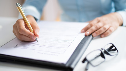 Na zdjęciu widać damskie dłonie, kobieta długopisem podpisuje dokument, obok leżą okulary