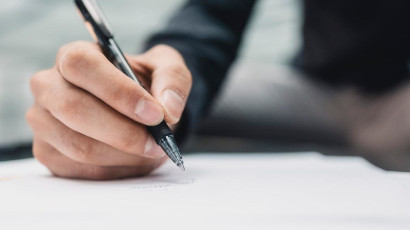 Na zdjęciu znajduje się dłoń trzymająca długopis podpisująca dokument.