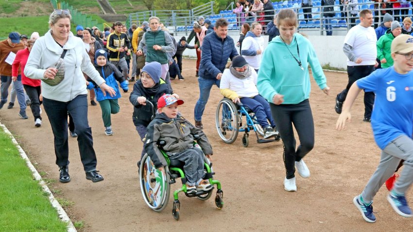  Na zdjęciu widać liczną grupę ludzi biegnących po bieżni stadionu, w tym 2 osoby na wózkach inwalidzkich