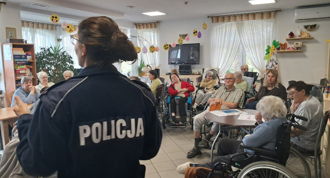 zdjęcie przedstawia policjantkę stojącą tyłem, podczas spotkania z seniorami. 