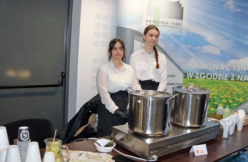 Dwie kobiety odpowiedzialne za bufet stoją przy palniku z dwoma garnkami.