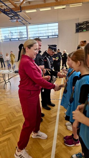 Zdjęcie przedstawia Wójta Gminy Gardeja Karolinę Nowak składającą uściski dzieciom stojącym w szeregu. W tle, obok niej widzimy Starostę Kwidzyńskiego Tomasza Frejnagiela oraz Prezesa Zarządu Oddziału Powiatowego ZOSP RP Tomasza Kazimierczyka. 