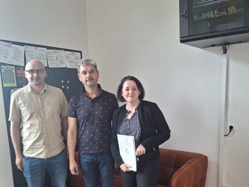 Zdjęcie przedstawia kobietę i dwóch mężczyzn stojących przed kanapą, obok tablicy z rysunkami, na ścianie wisi jedno z zamontowanych urządzeń