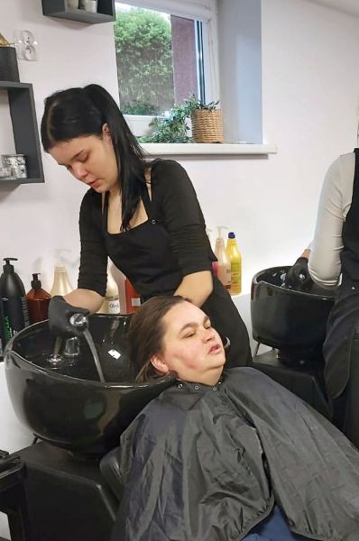 Wychowanka Młodzieżowego Ośrodka Wychowawczego im. Janusza Korczaka w Kwidzynie myje głowę osobie z niepełnosprawnością w pracowni fryzjerskiej