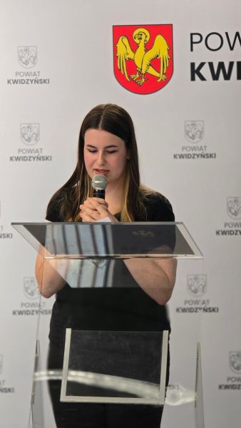Na zdjęciu widać kobietę przemawiającą na tle ścianki powiatu kwidzyńskiego Na zdjęciu widać kobietę przemawiającą na tle ścianki powiatu kwidzyńskiego