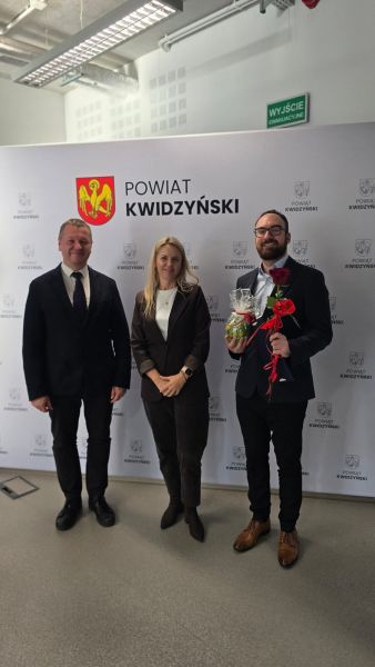 Na zdjęciu widać starostę kwidzyńskiego oraz kobietę i mężczyznę pozujących na tle ścianki powiatu kwidzyńskiego Na zdjęciu widać starostę kwidzyńskiego oraz kobietę i mężczyznę pozujących na tle ścianki powiatu kwidzyńskiego