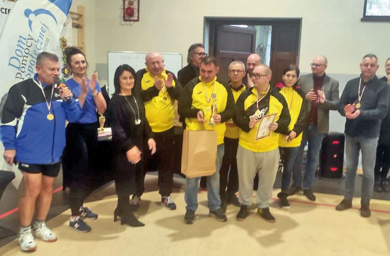 Zdjęcie grupowe wyróżnionych zawodników i zawodniczek turnieju ping-ponga stołowego wraz z prowadzącymi zawody.