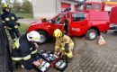 Czterech strażaków w akcji: dwóch przeszukuje apteczkę, jeden rozmawia przez radio, a drugi zabezpiecza osobę poszkodowaną w wypadku samochodowym.