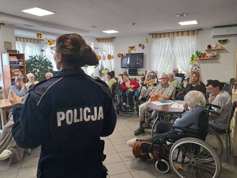 zdjęcie przedstawia policjantkę stojącą tyłem, podczas spotkania z seniorami. 