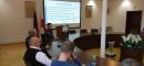 Trzecia grupa szkoleniowa uczestnicząca w szkoleniu na miejscach siedzących przy okrągłym stole konferencyjnym wraz z osobą prowadzącą szkolenie omawiającą program szkolenia