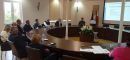 Trzecia grupa szkoleniowa uczestnicząca w szkoleniu na miejscach siedzących przy okrągłym stole konferencyjnym wraz z osobą prowadzącą szkolenie omawiającą szczegółowe tematy szkolenia