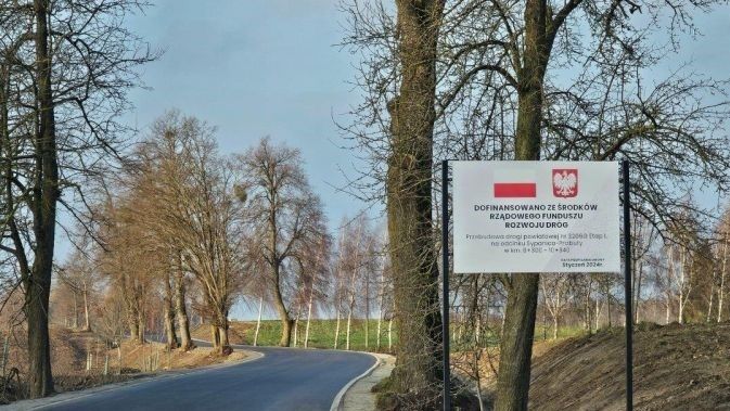Wyremontowany fragment drogi Prabuty-Sypanica oraz tablica informacyjna o dofinansowaniu inwestycji ze środków Rządowego Funduszu Rozwoju Dróg.